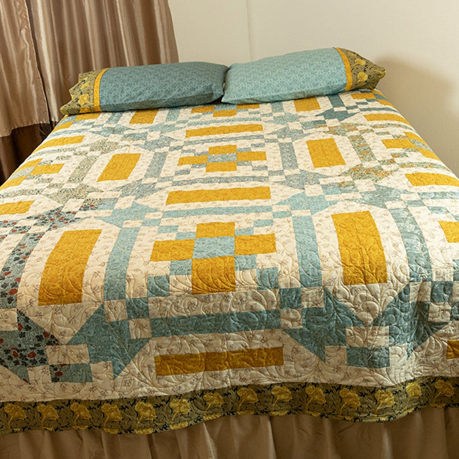 Bed with a patterned quilt in a room with curtains and carpet.