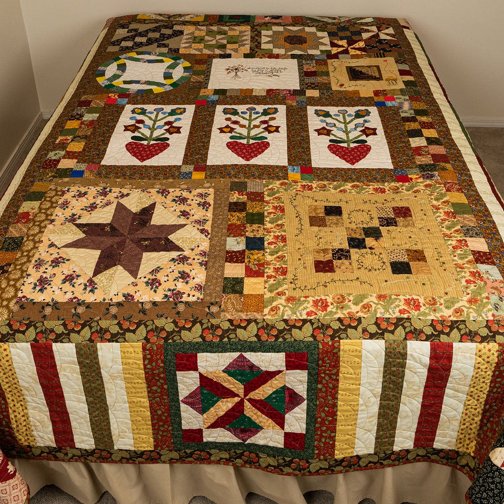 Quilt with various patterns on a bed in a room.