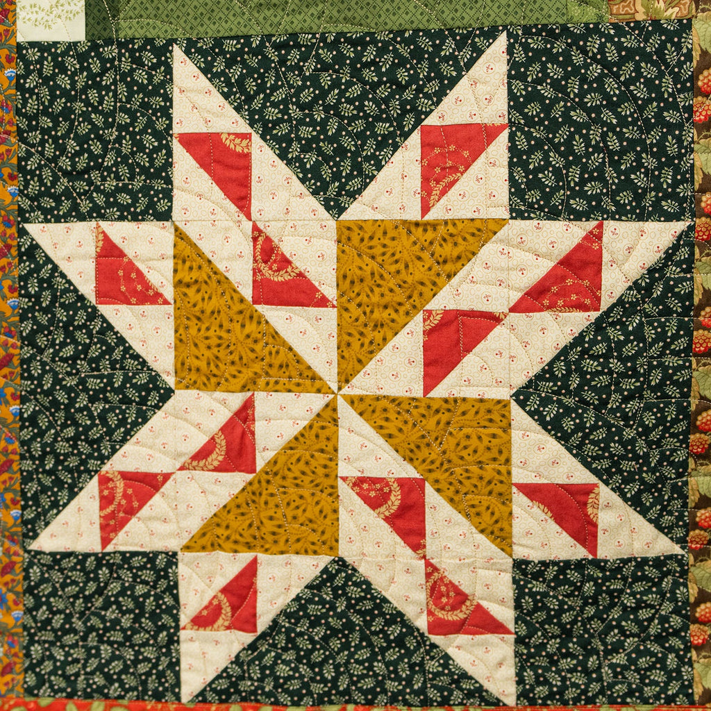 Quilt with star pattern featuring red, yellow, and white triangles on a green background.