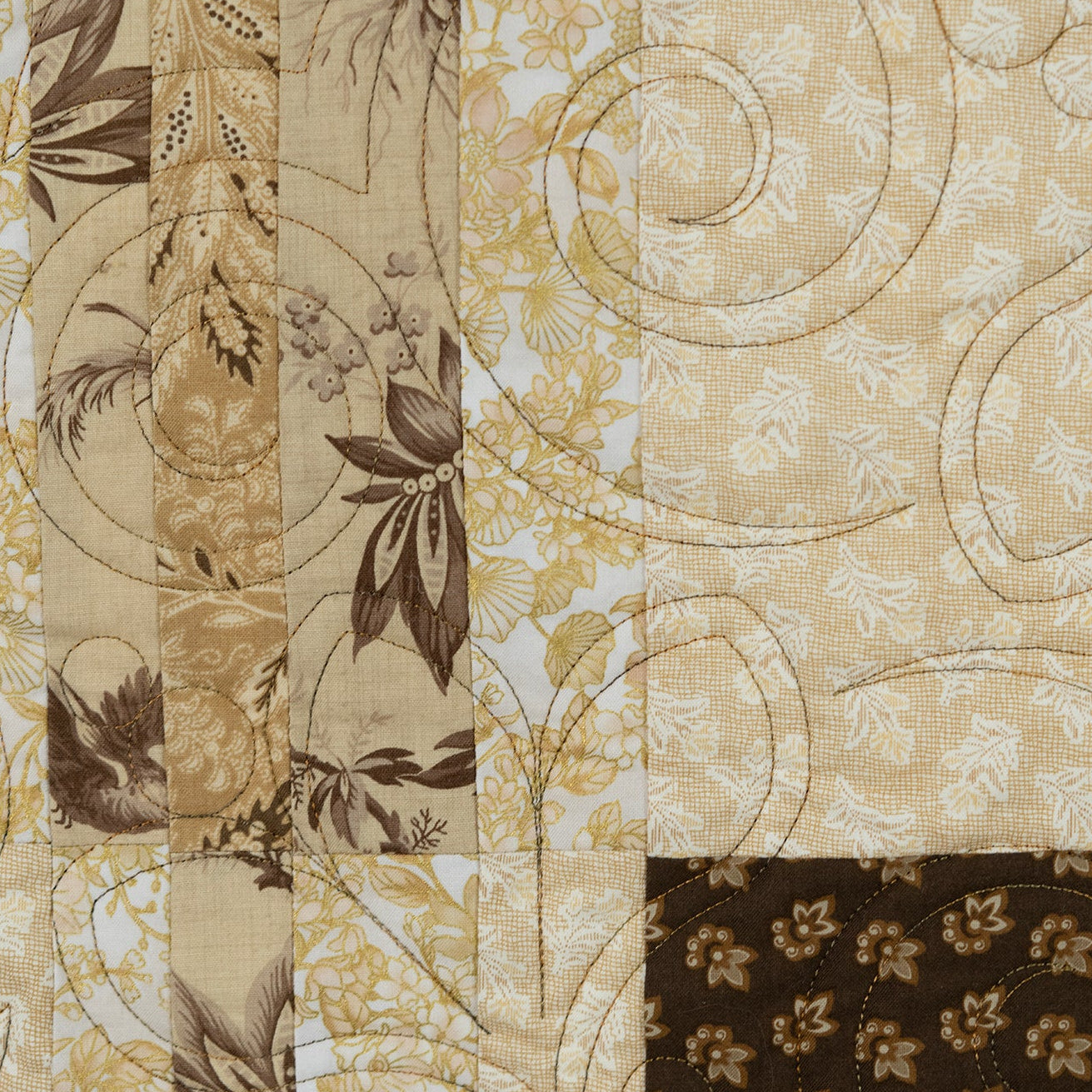 Close-up of a quilt with floral and leaf patterns in beige, brown, and white.
