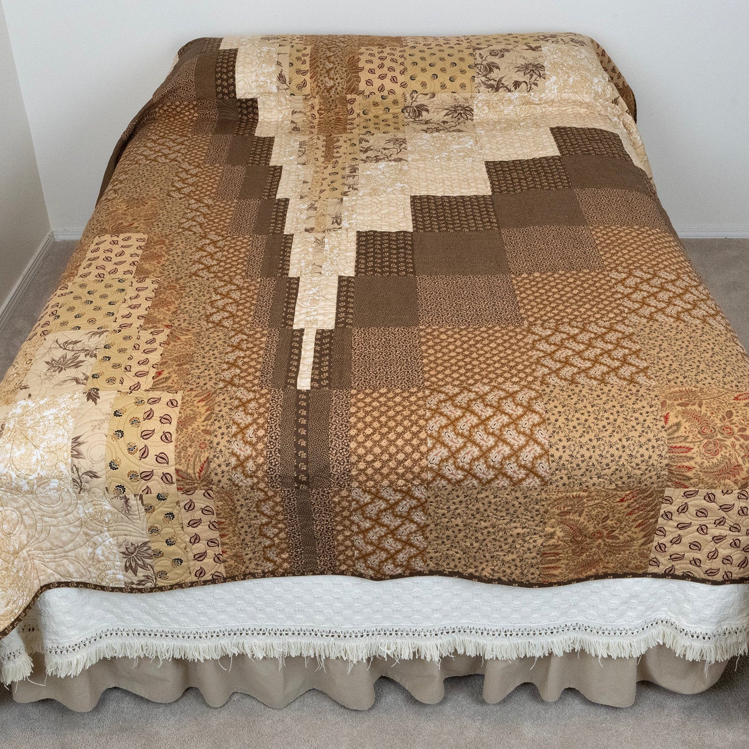 Patchwork quilt with brown and beige patterns on a bed.