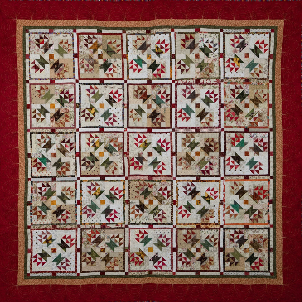 A square quilted textile with a red border and a grid of small patchwork blocks featuring geometric star and triangle motifs in beige, brown, red, green, and black.