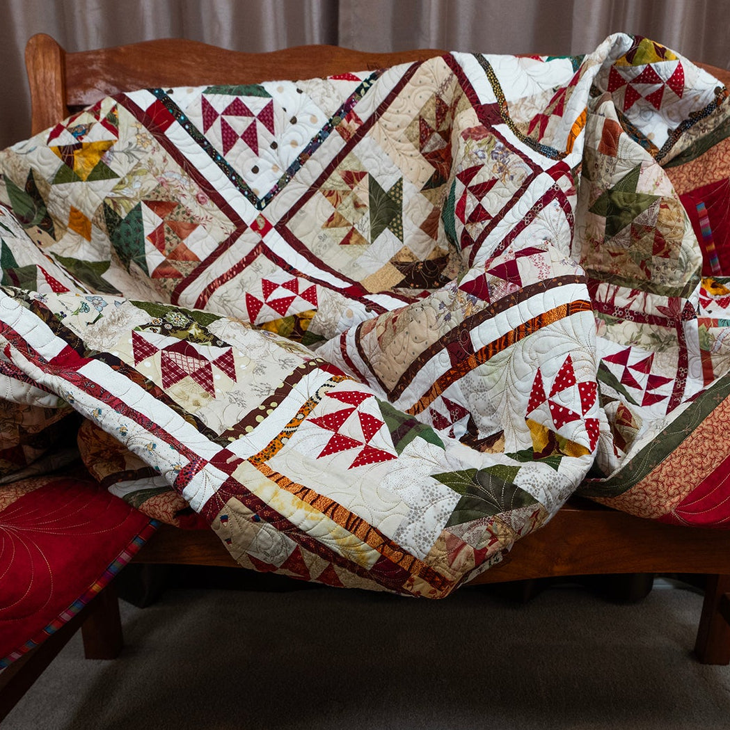 A multicolor geometric quilt draped over a wooden bench in an indoor room setting, with red quilted ends and a cream base fabric.