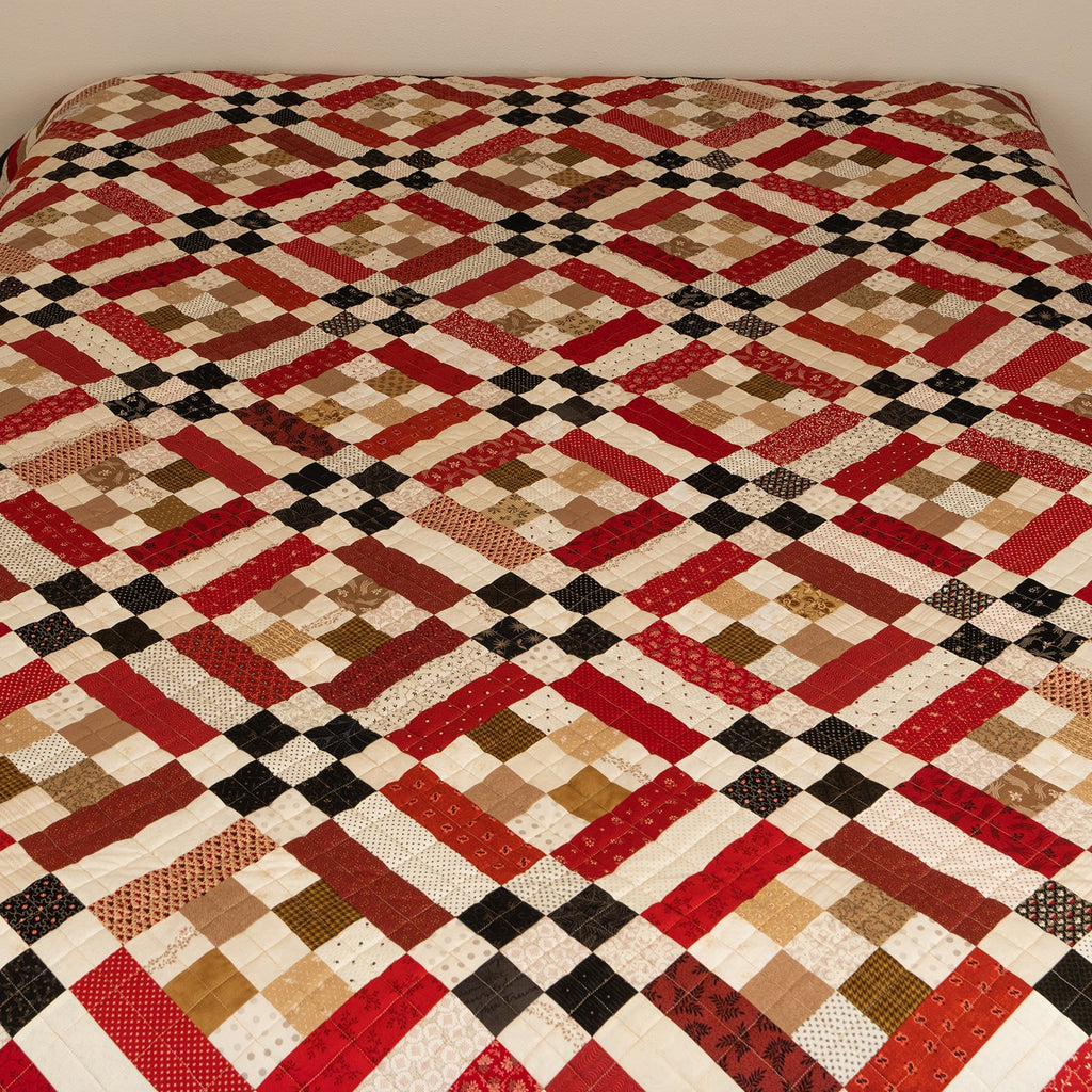 Quilt with a geometric pattern on a bed against a plain wall