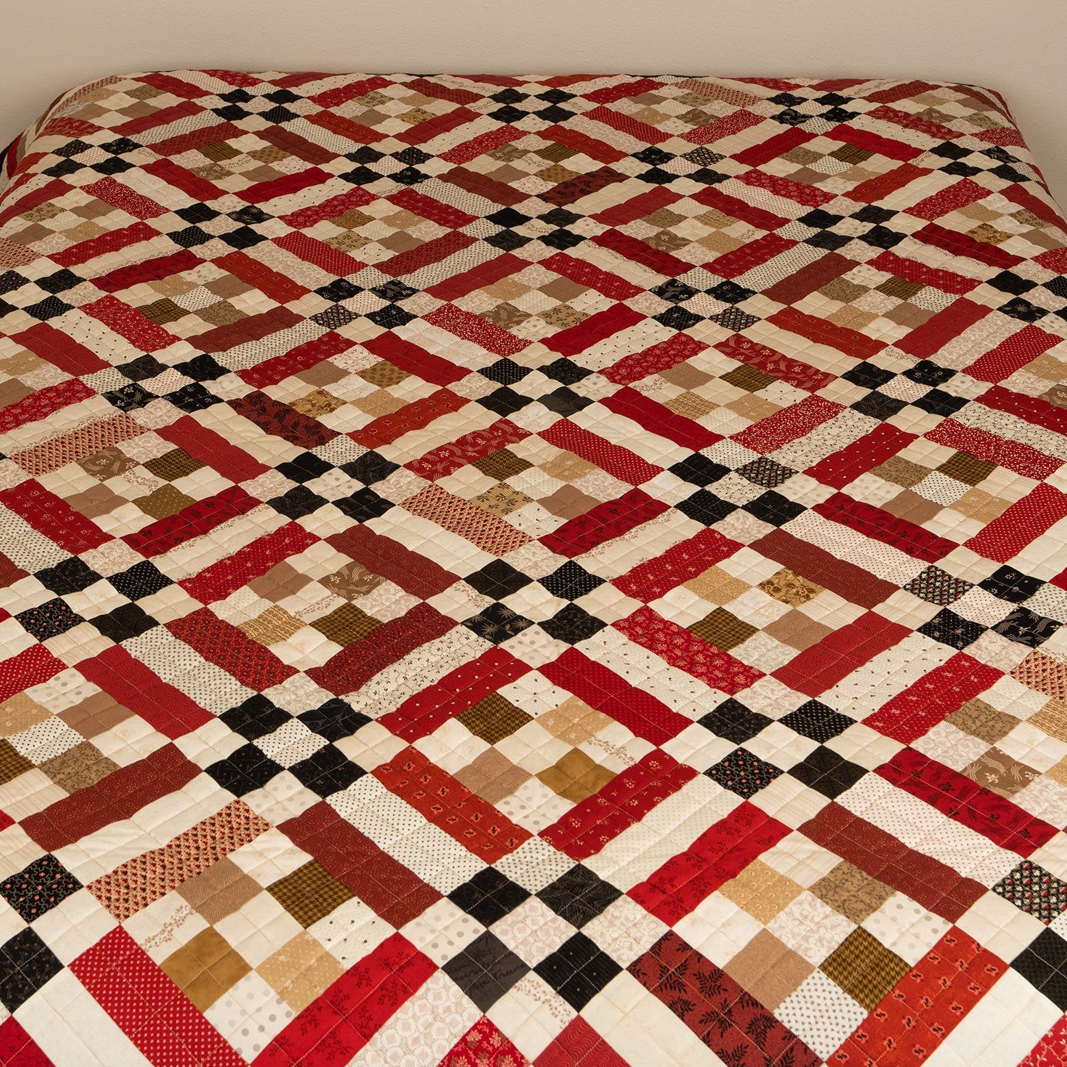 Quilt with a geometric pattern on a bed against a plain wall