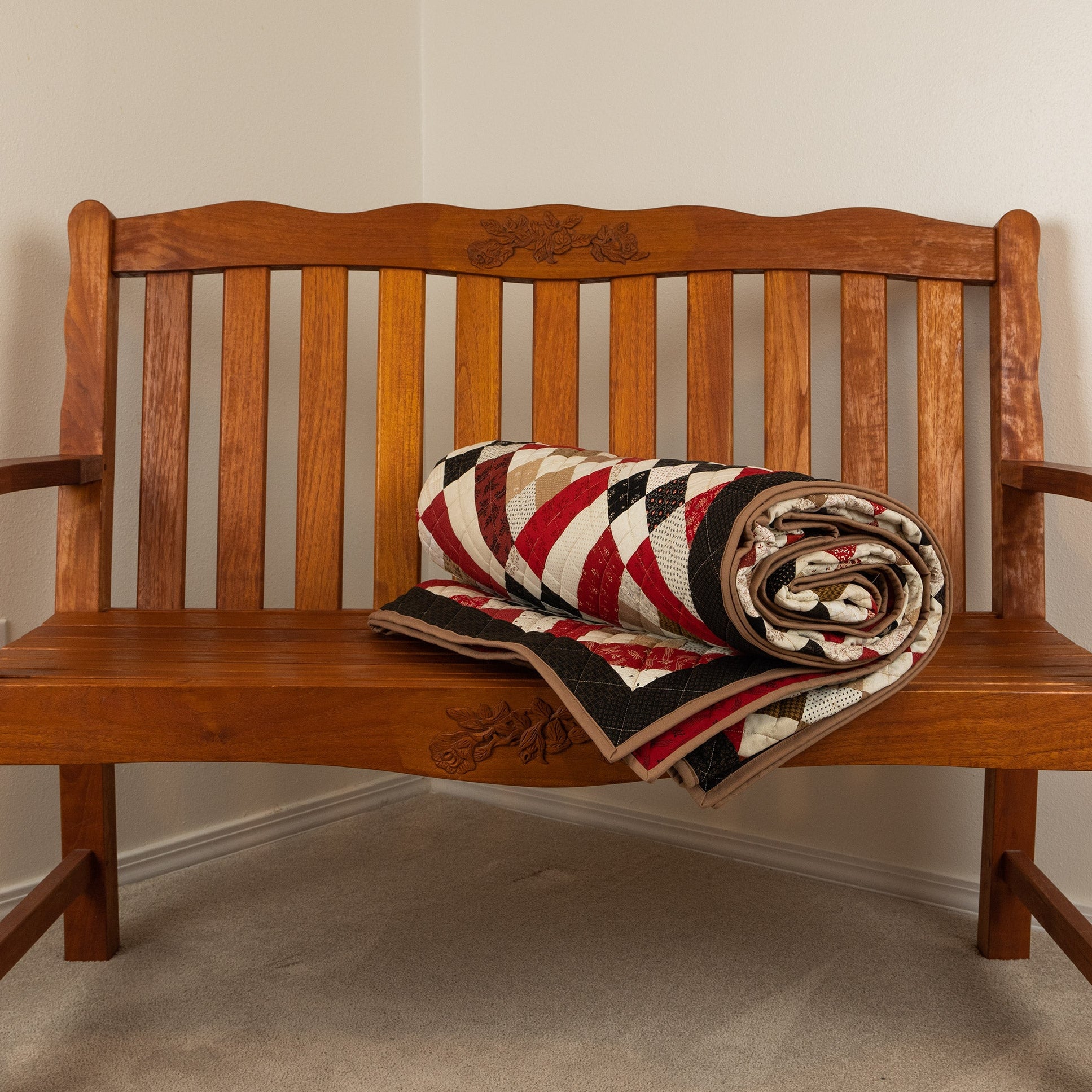 Wooden bench with a quilt draped over it against a plain wall.
