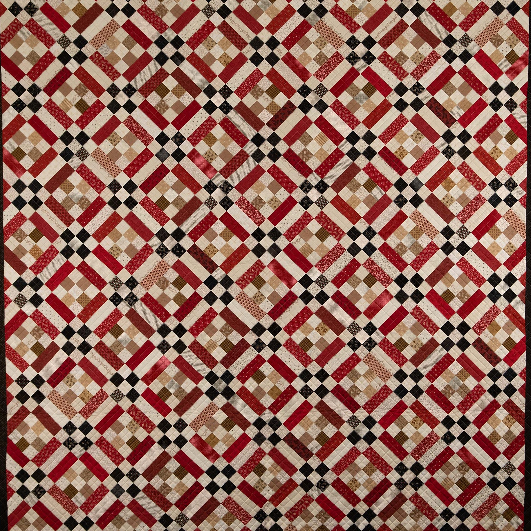 Quilt with a geometric diamond pattern in red, beige, and black