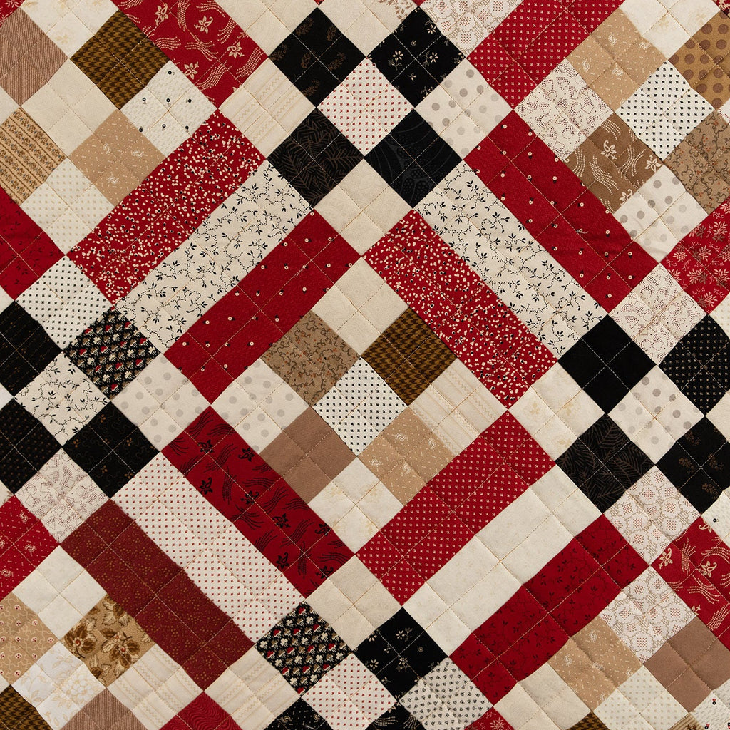Patchwork quilt with a diamond pattern in red, brown, black, and beige.