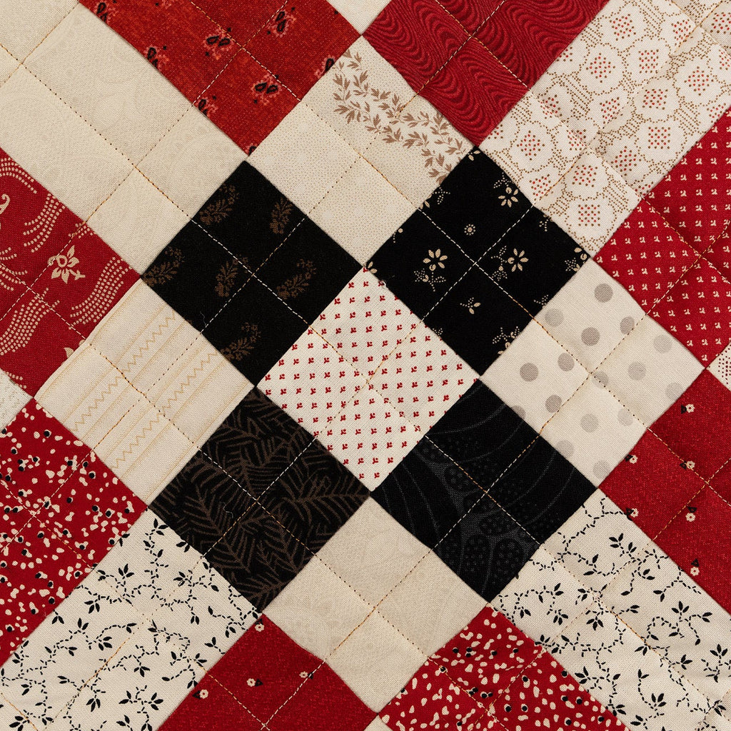 Quilt with a patchwork pattern featuring red, black, and beige fabrics.