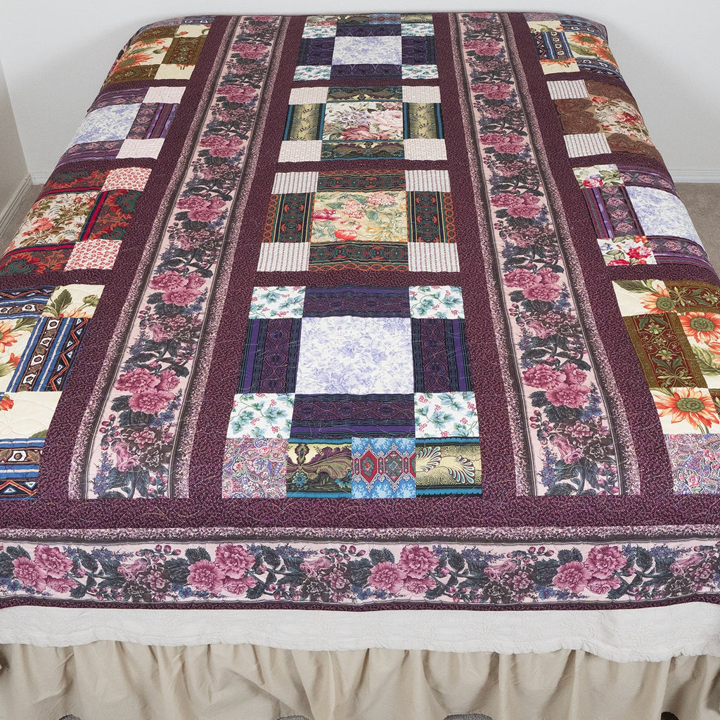 Patchwork quilt with floral patterns draped over a bed in a room.