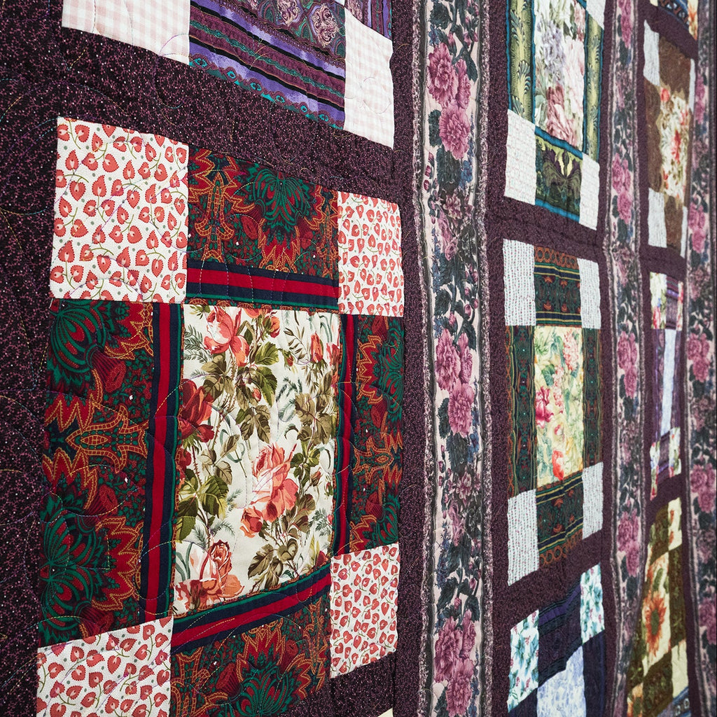 Quilt with floral and patchwork patterns displayed on a wall.