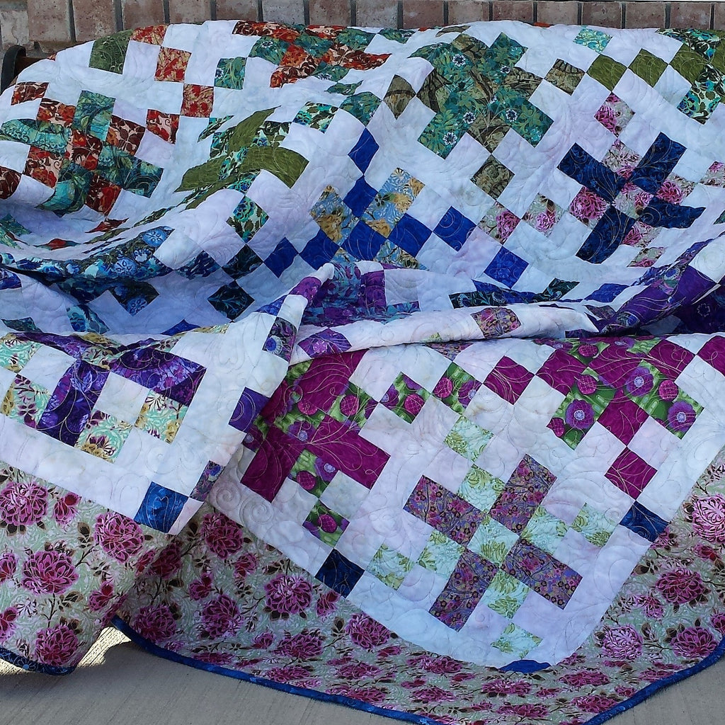 Colorful quilt with a patchwork design draped over a chair against a brick wall.