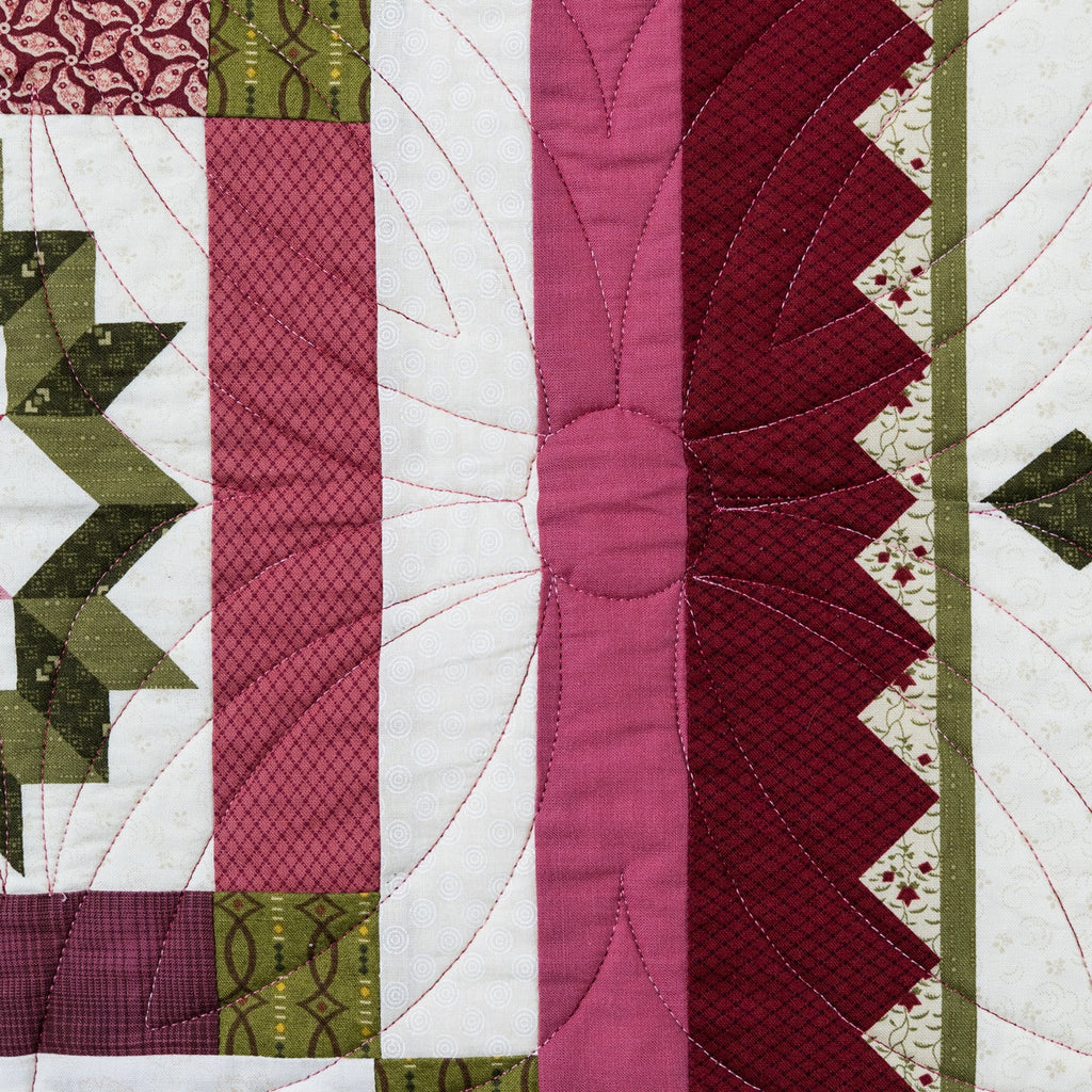 Close-up of a quilt with geometric patterns in green, pink, and red on a white background.