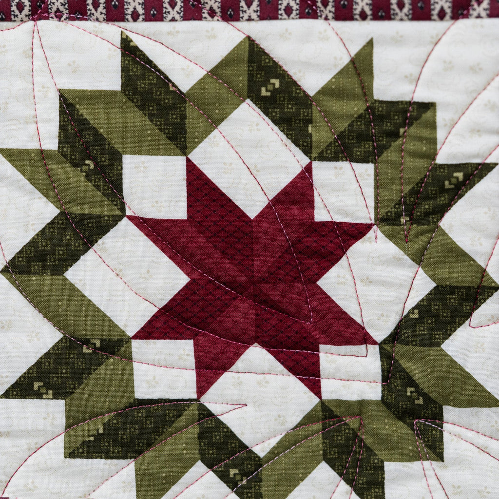 Quilt block with star pattern in green, red, and white on a purple background