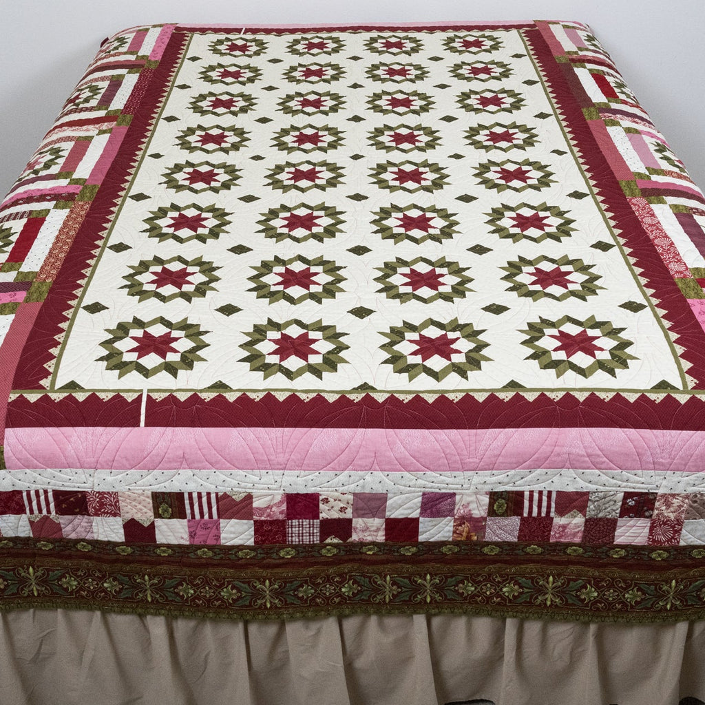 Quilt with a geometric pattern draped over a bed in a room.