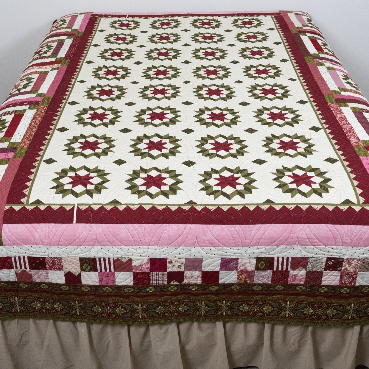 Quilt with a geometric pattern draped over a bed in a room.