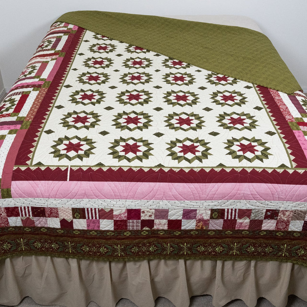 Quilt with a geometric pattern on a bed against a white wall.