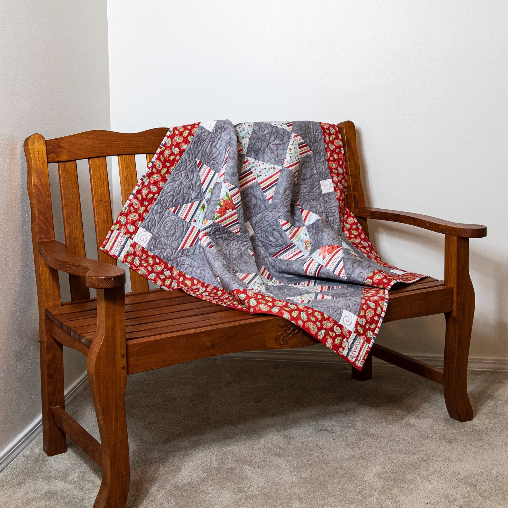 Wooden bench with a quilt draped over it against a plain wall.