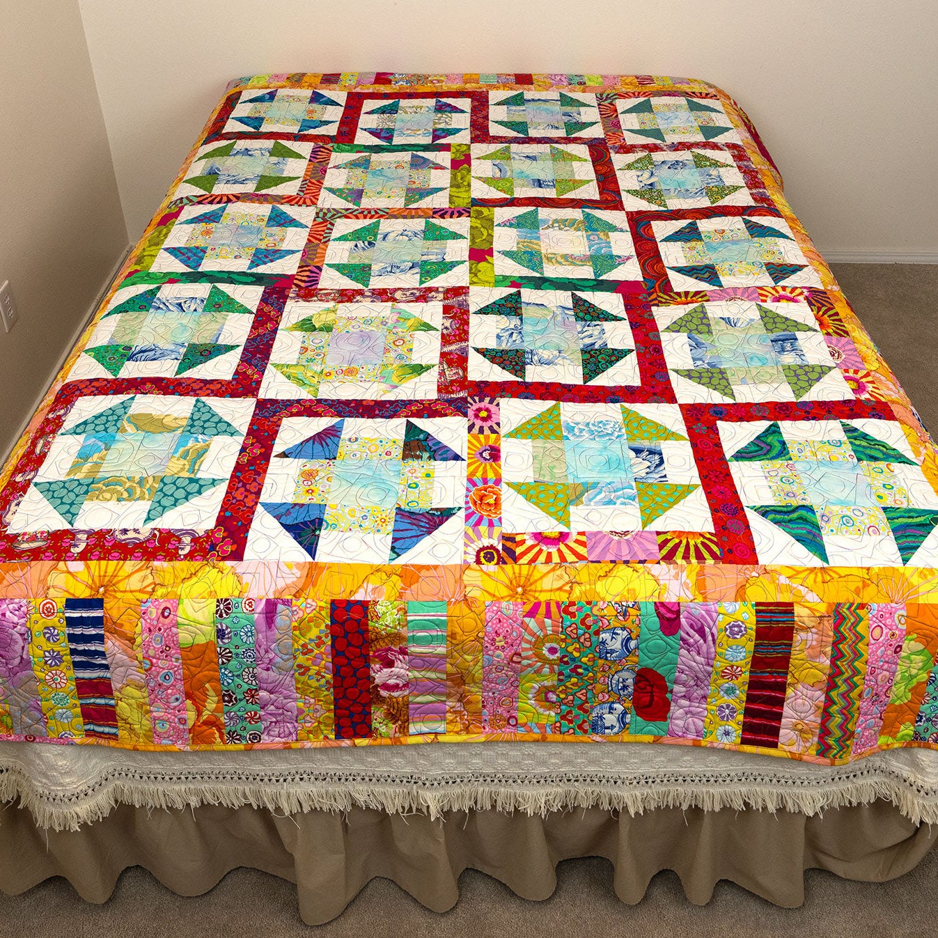 Colorful quilt on a bed in a room with neutral walls.