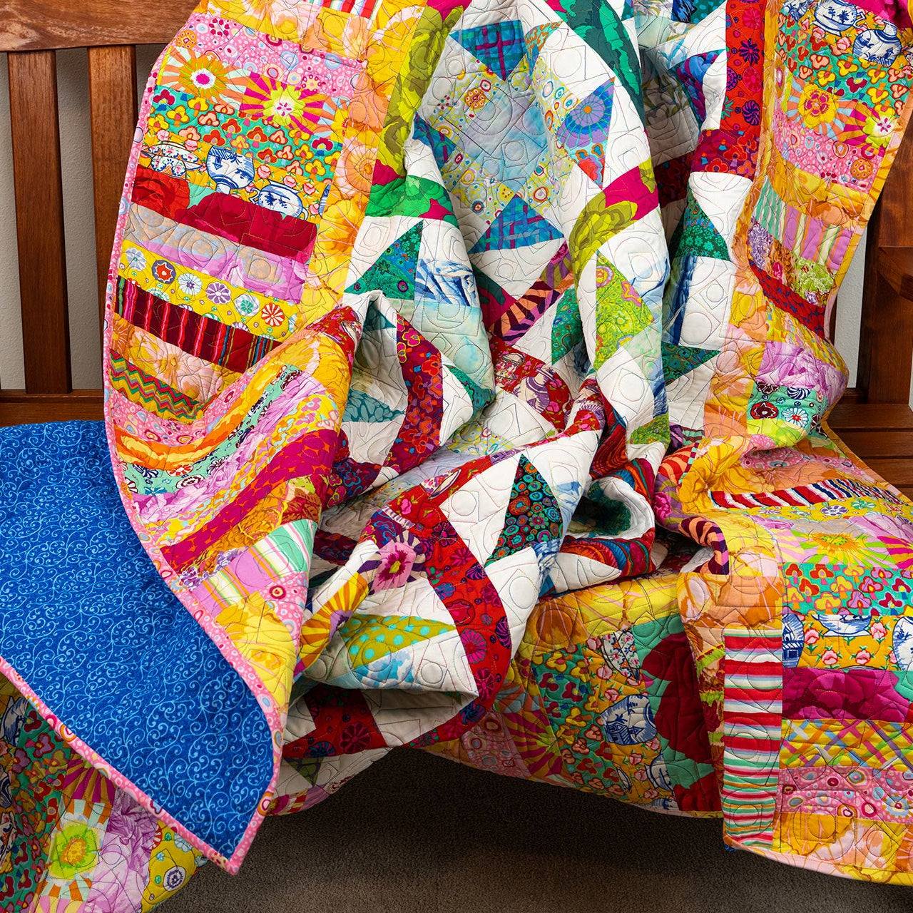 Colorful quilt draped over a wooden chair against a plain wall.