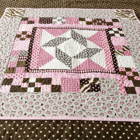 Wall hanging in a floral and geometric pattern in pink and brown laid on a pink and brown polkadot print. 