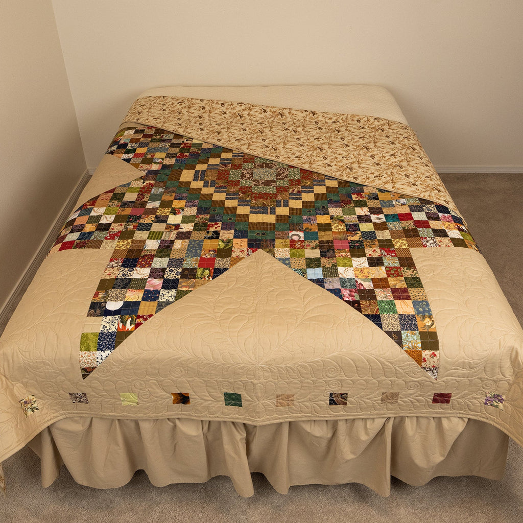 Bed with a patchwork quilt in a room with beige carpet and walls.
