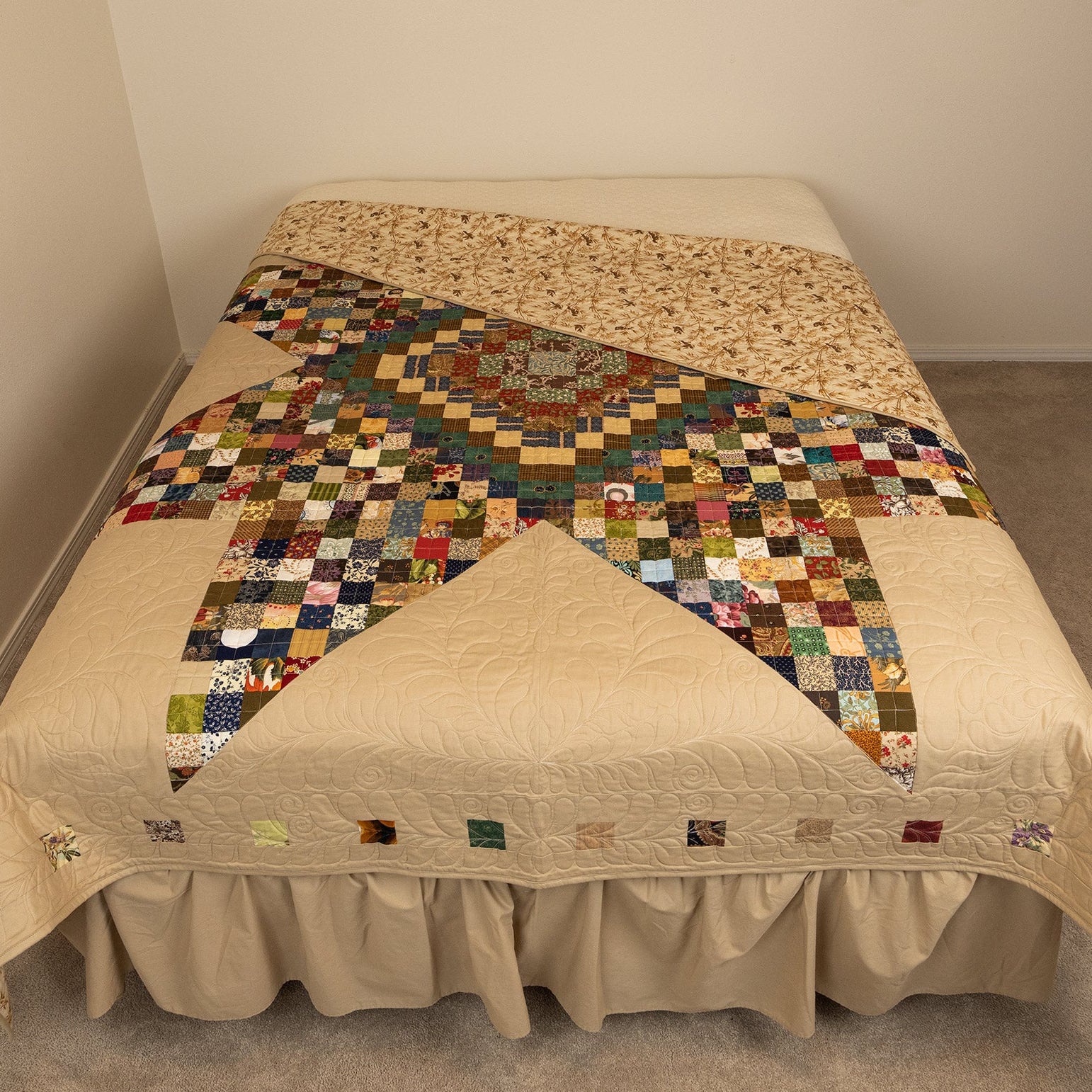 Bed with a patchwork quilt in a room with beige carpet and walls.