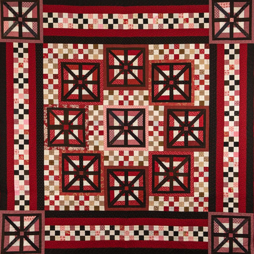 A square quilt with a traditional Southwestern or geometric pattern, featuring red, black, and cream checkered blocks and starburst motifs.