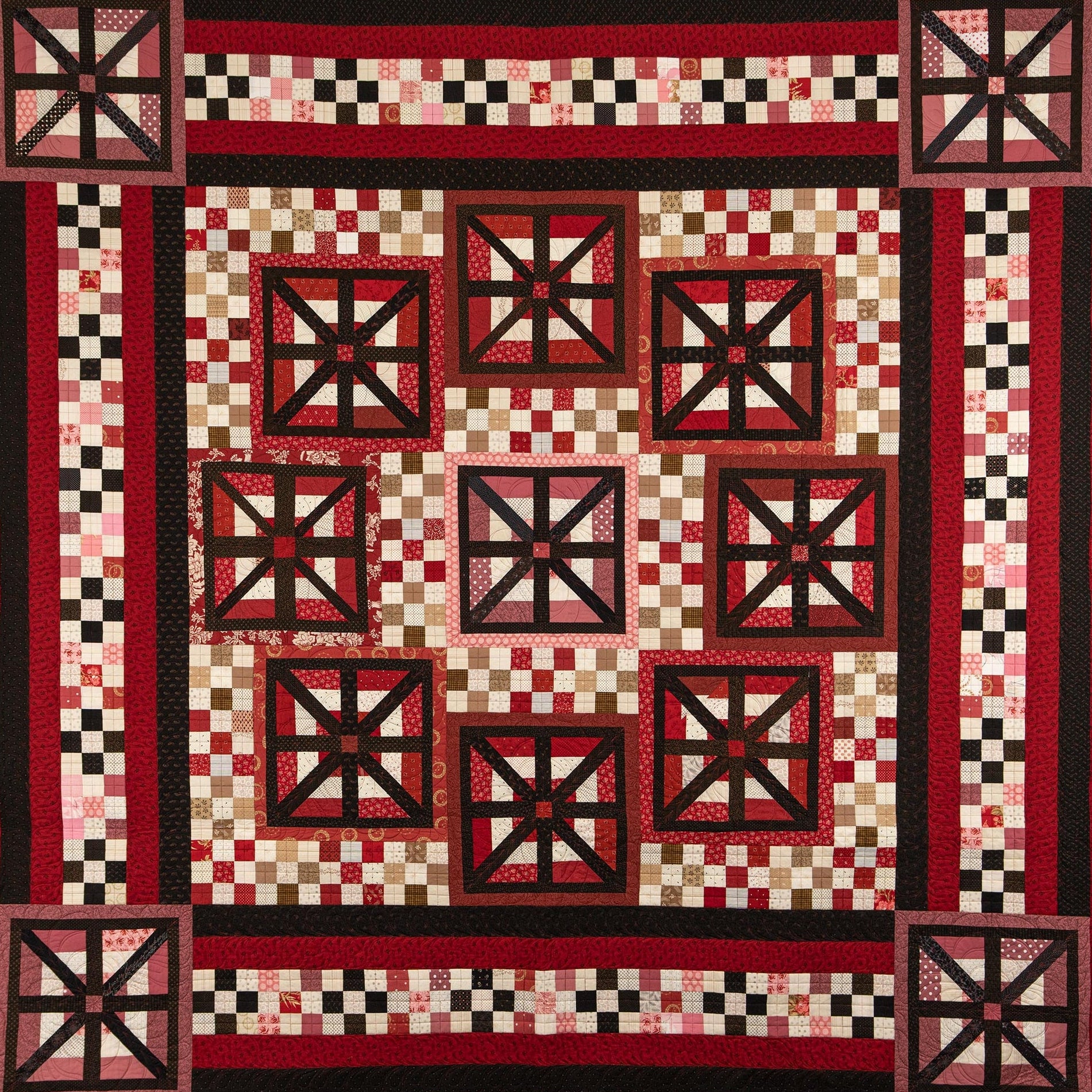 A square quilt with a traditional Southwestern or geometric pattern, featuring red, black, and cream checkered blocks and starburst motifs.
