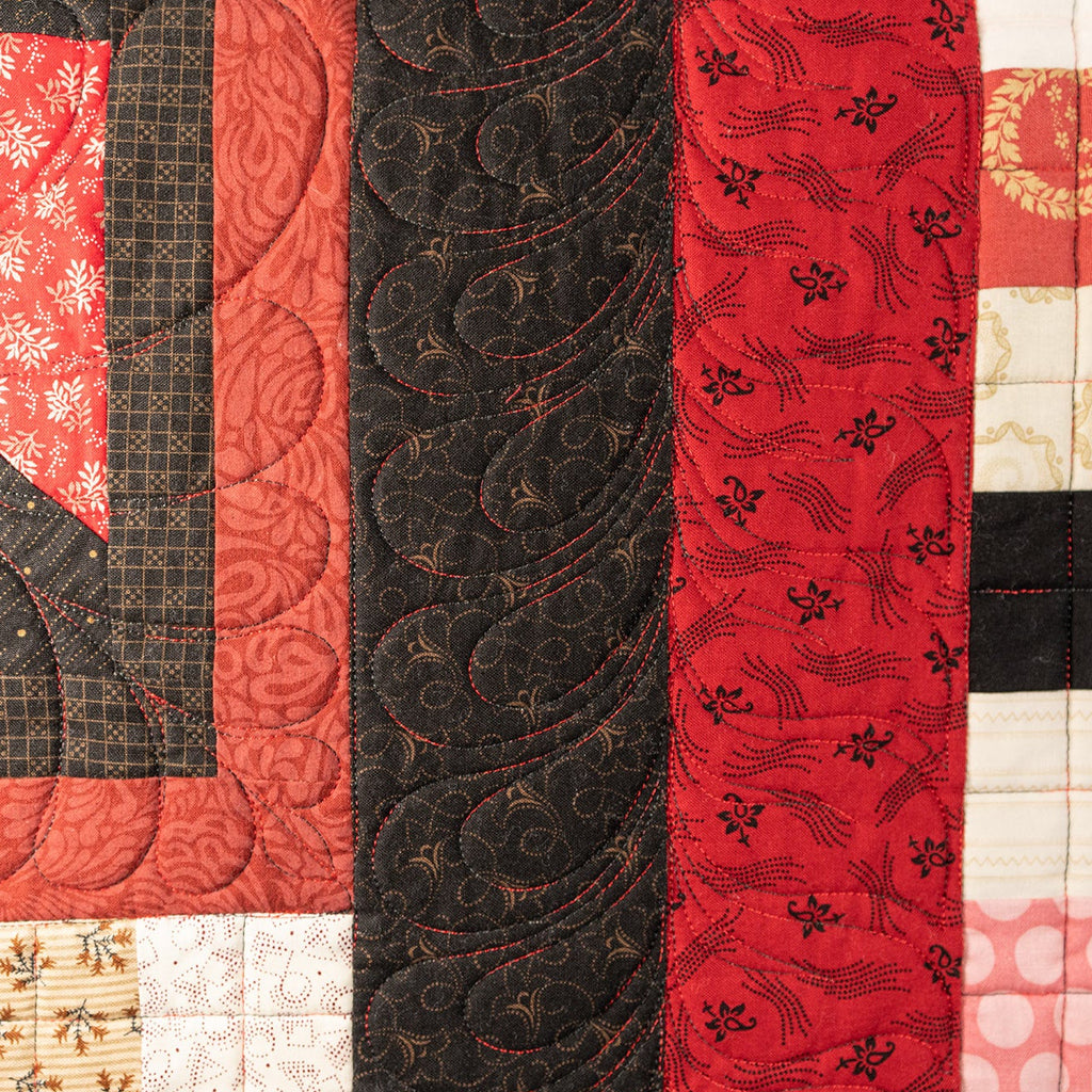 A close up of a quilt in black and red with various floral prints. 