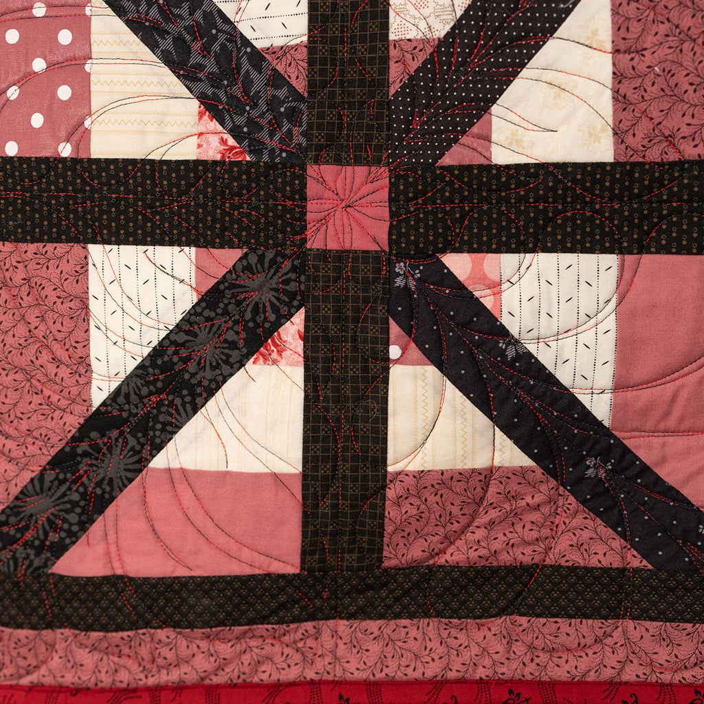 A square patchwork quilt featuring a Union Jack-inspired design with dark brown and black striped borders, dusty pink polka dot sections, and cream-colored blocks with stitched details.