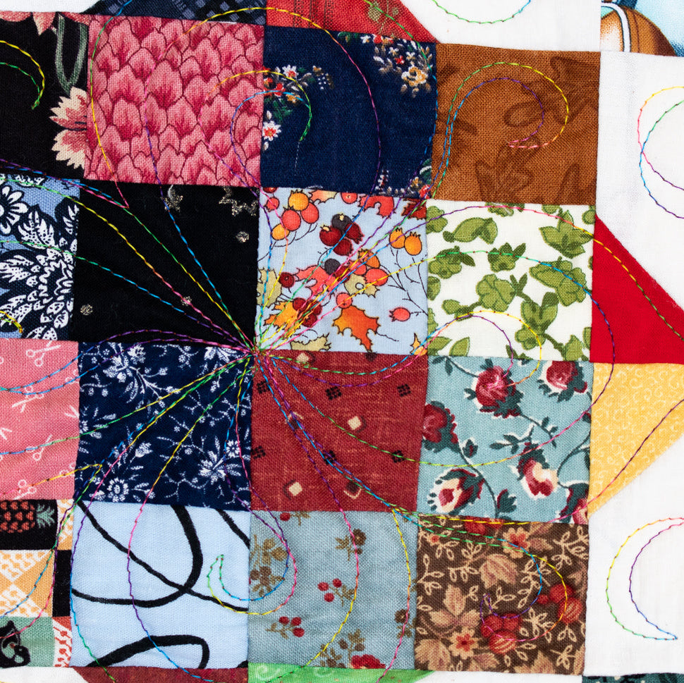 A close-up of a colorful patchwork quilt with stitched geometric and floral patterns, featuring various fabric squares in pink, blue, red, green, yellow, and brown.