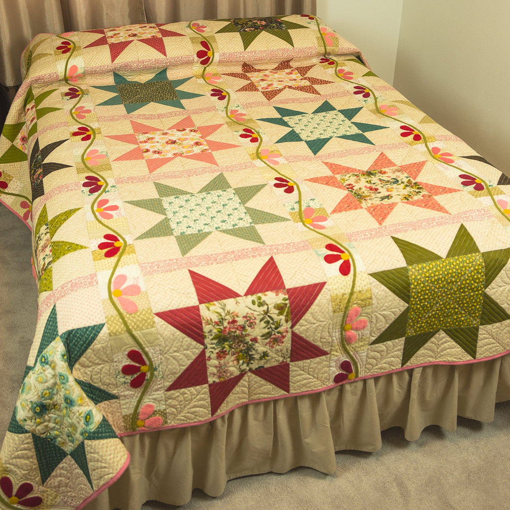 A multicolor patchwork quilt with star and floral block patterns, draped over a bed with a beige ruffled skirt in a bedroom setting.