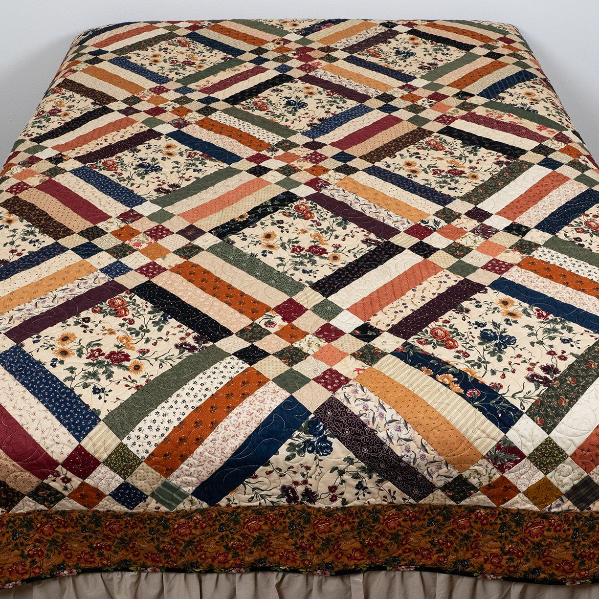 Quilt with a geometric pattern draped over a bed in a room.