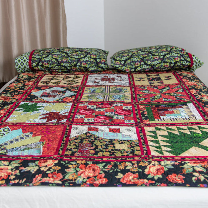 A colorful patchwork quilt with a floral border and two matching patterned pillows on a bed in a bedroom setting.