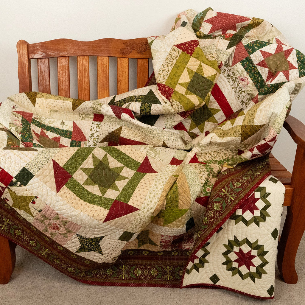 Patterned quilt in green, red and neutral tones laid on a wooden bench