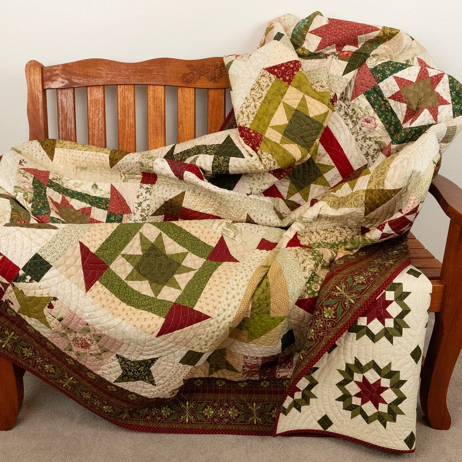 Patterned quilt in green, red and neutral tones laid on a wooden bench