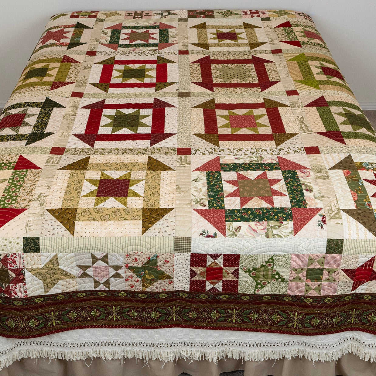 Churn dash patterned quilt in red, green and neutral tones laid out on a bed