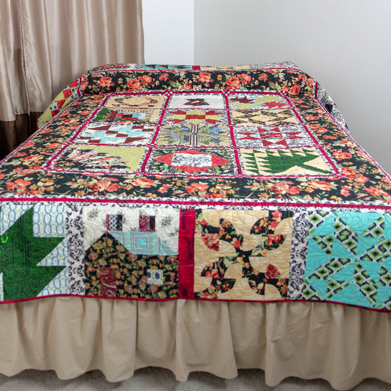 A colorful patchwork quilted bedspread with a beige ruffled bed skirt, shown on a bed in a bedroom setting with beige curtains and a wooden nightstand.