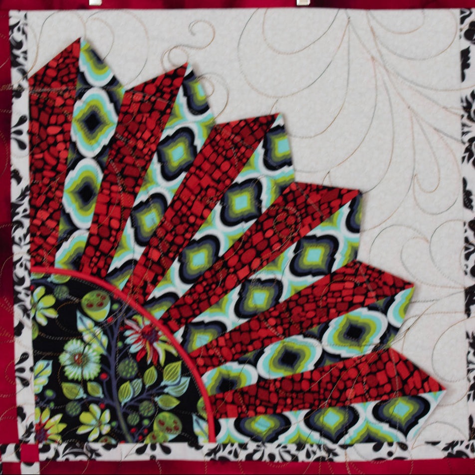 A close-up of a quilt with a large fan-shaped patch design in red, black, green, and cream.