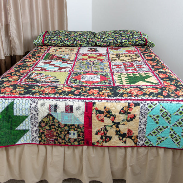A colorful patchwork quilted bedspread with matching pillowcases on a bed in a bedroom setting with beige curtains, a wooden nightstand, and a lamp.