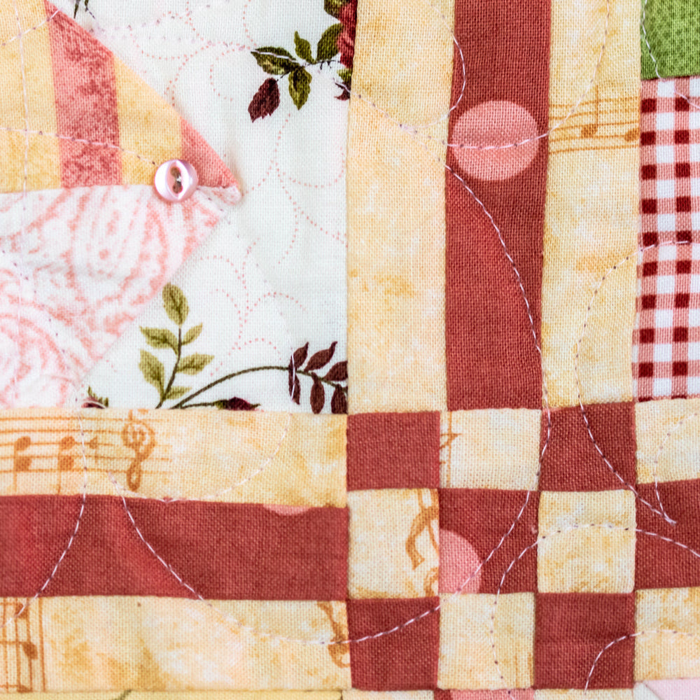 Close-up of a patchwork quilt showing various fabric patterns including stripes, floral prints, musical notes, gingham, and checks in muted red, cream, pink, and green.
