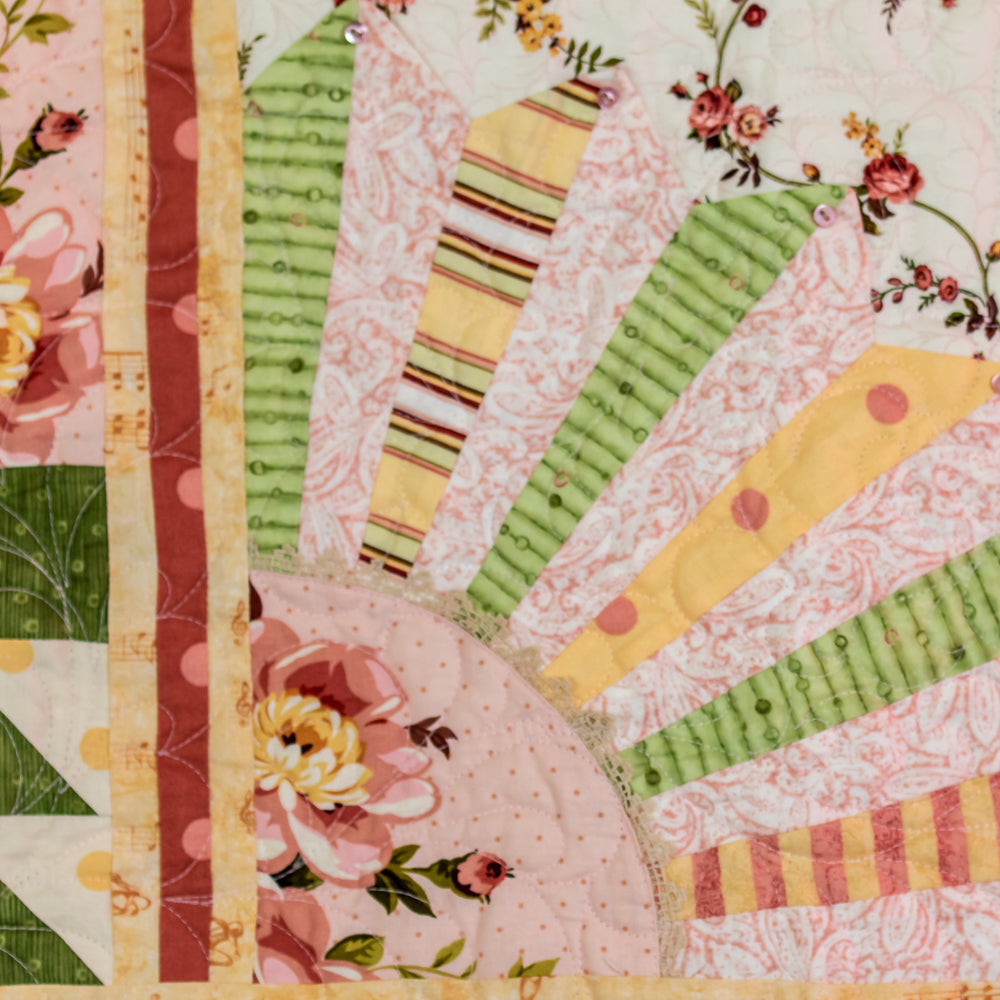 A close-up of a handmade quilted textile featuring a colorful patchwork design with floral and striped fabric segments in pink, green, yellow, and red.