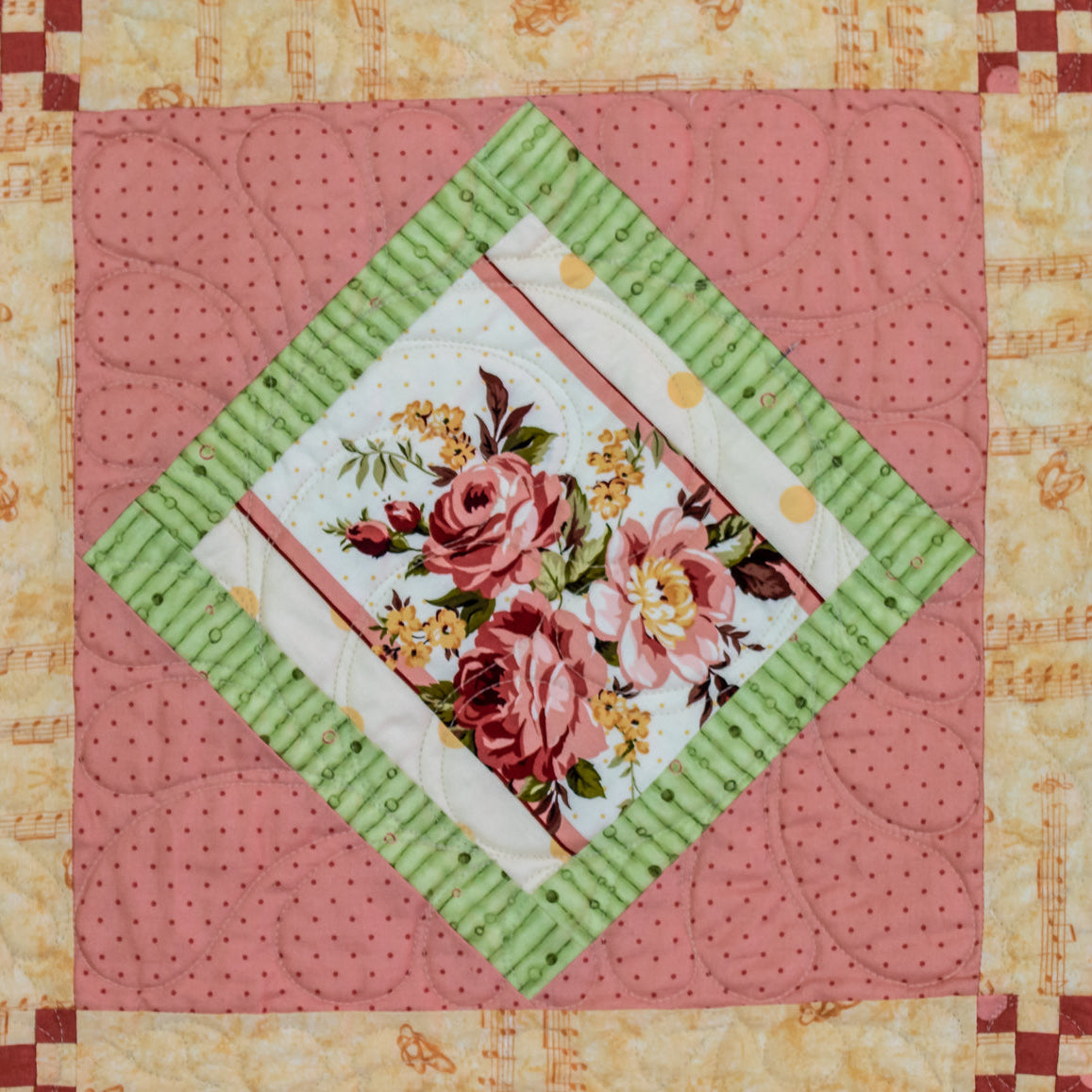 Quilt block with a large floral print in the centre in a diamond shape with a pink polkadot and music note border.