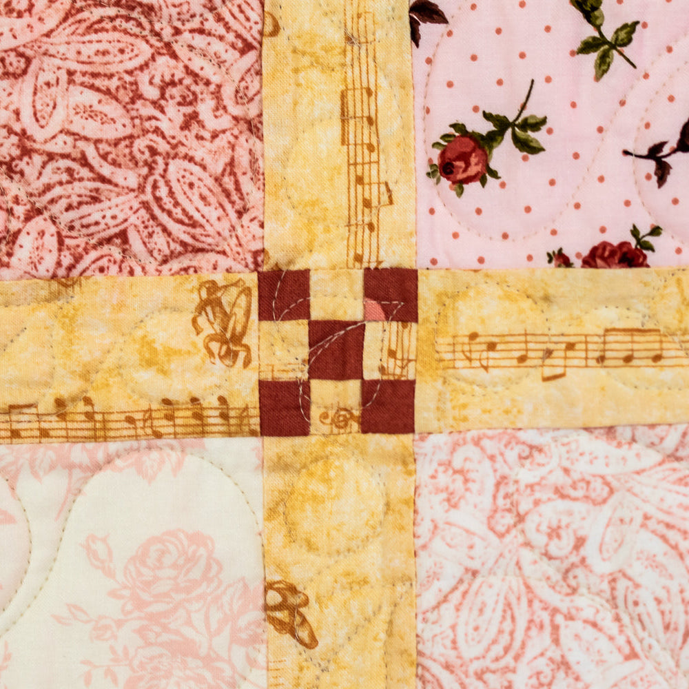 Quilt block with a criss cross stitched patch with a music note print surrounded by a floral print.