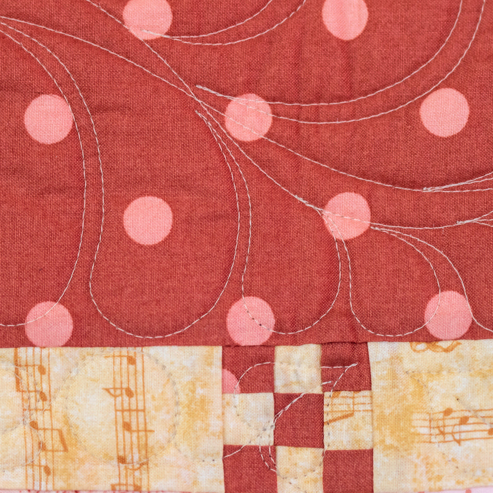 Close up of quilt stitching with a polkadot print and music note print. 