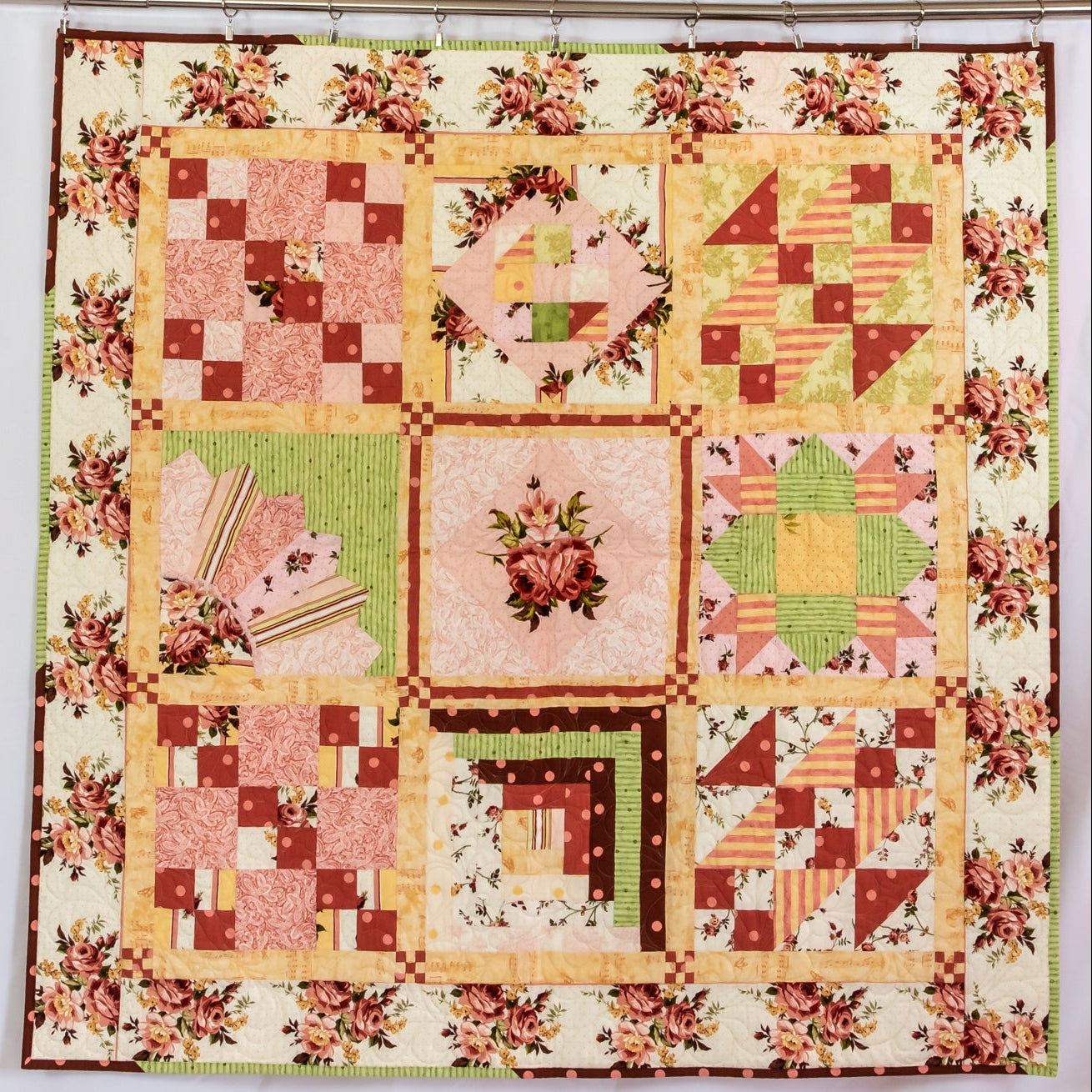Quilted wall hanging in a checkered layout with various prints in each block, all with a floral border. 