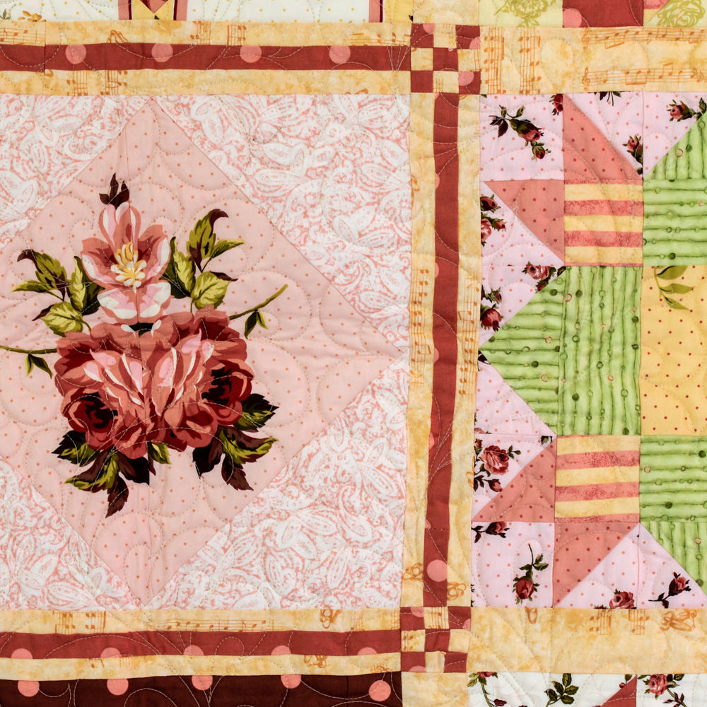 Quilt block close up with various floral patterns in pinks, peach, neutral and green tones. 