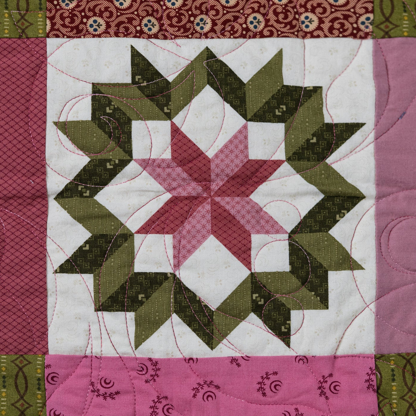 Quilt block in a star patter in green and pink with patterned borders