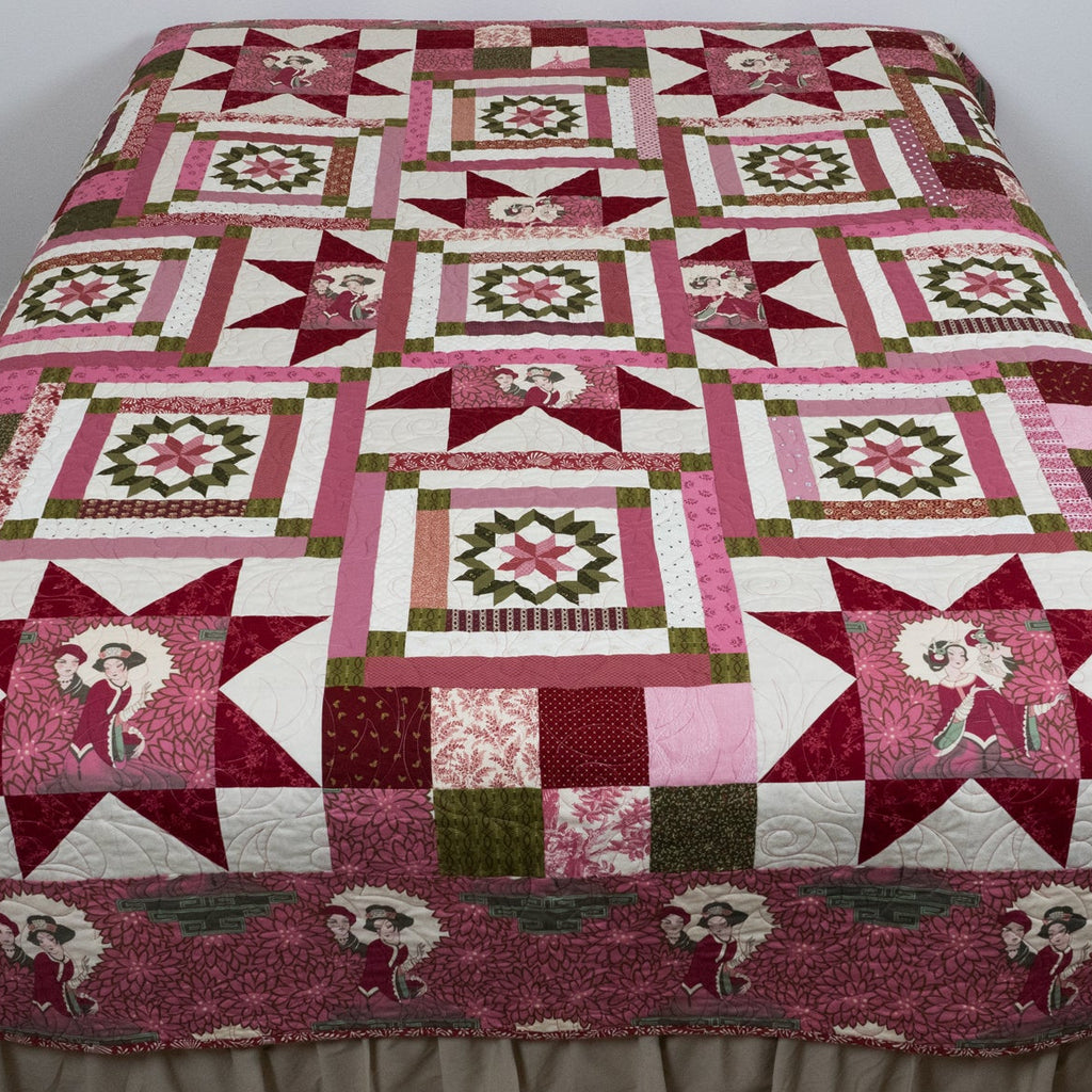 Pink geometric and star printed quilt with empress figures around the border laid out on a bed